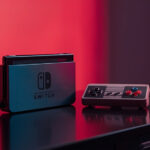 Console de videogame moderno sobre mesa de madeira escura ao lado de controle clássico em iluminação cinematográfica de estúdio