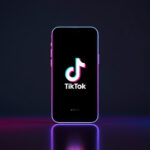 Smartphone moderno na vertical mostrando a interface do aplicativo TikTok com iluminação de estúdio em tons de rosa e azul
